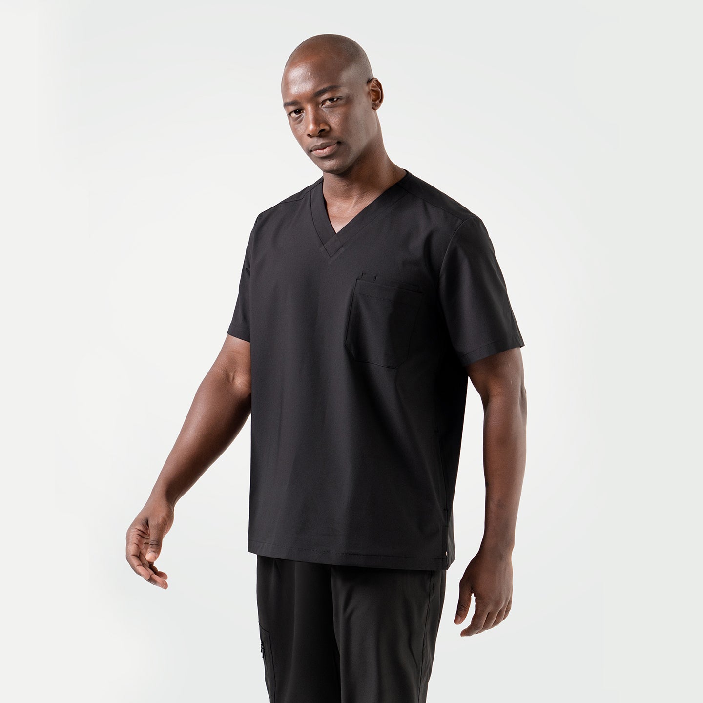Image of A smiling male model dressed in an Eco Black 3 Pocket scrub top, standing in a relaxed pose.